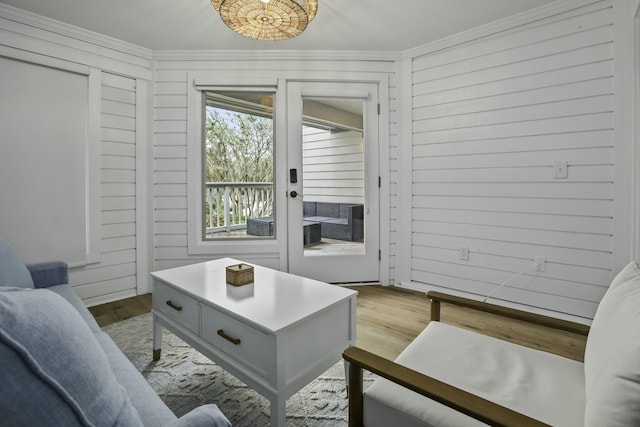 living room with crown molding, light wood-type flooring, and wood walls