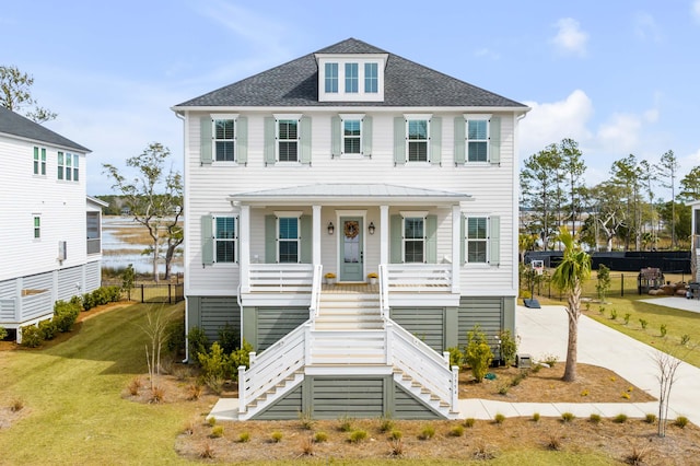 coastal home with a front lawn, a porch, fence, stairway, and roof with shingles