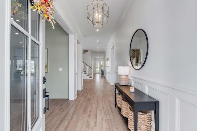 entryway with light wood-type flooring, an inviting chandelier, wainscoting, a decorative wall, and stairs