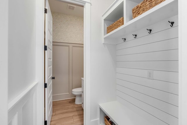 mudroom with light wood-type flooring, visible vents, wainscoting, and a decorative wall