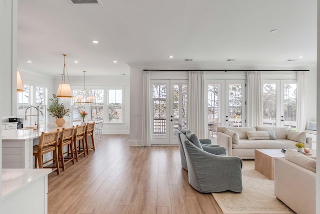 living room with baseboards, ornamental molding, recessed lighting, light wood-style flooring, and french doors