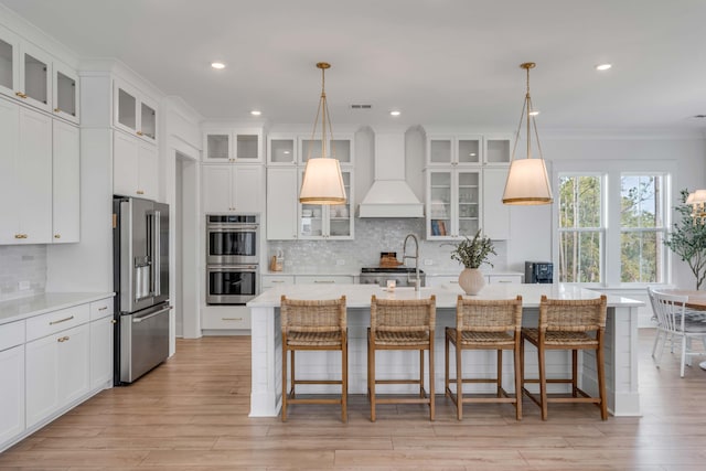 kitchen featuring visible vents, a kitchen island with sink, custom range hood, appliances with stainless steel finishes, and light countertops