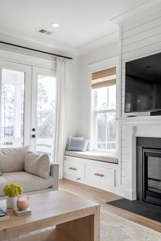 living area featuring visible vents, light wood-style flooring, ornamental molding, french doors, and a large fireplace