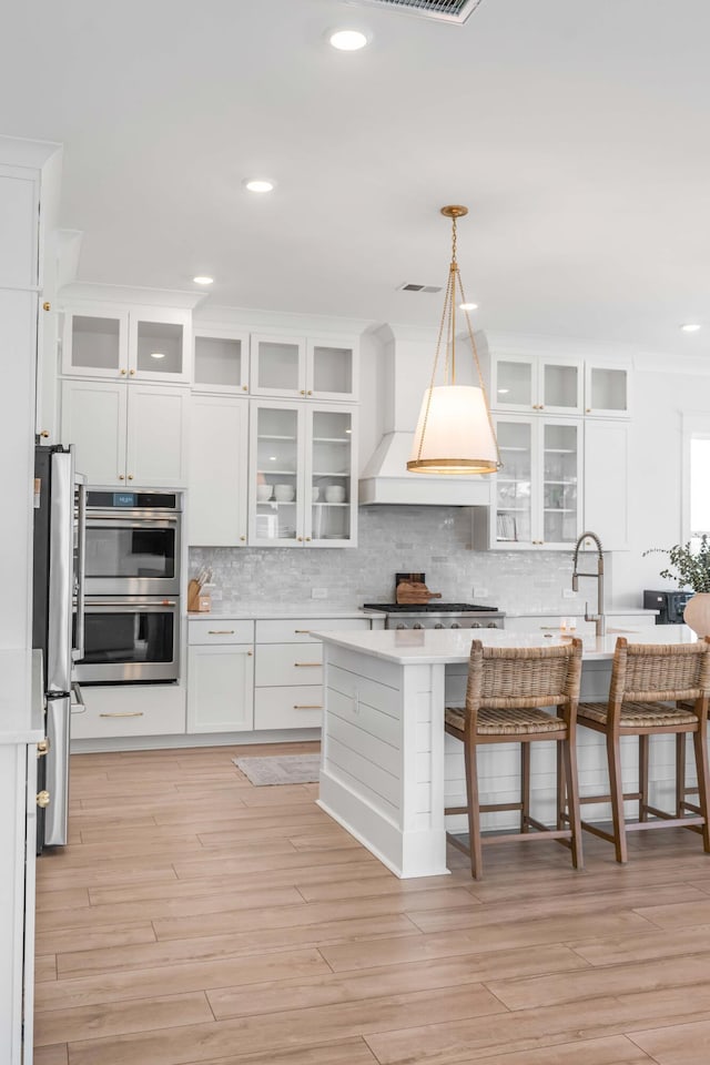 kitchen with visible vents, backsplash, light countertops, custom range hood, and appliances with stainless steel finishes