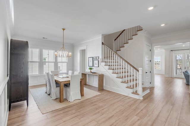 dining room featuring stairway, light wood finished floors, ornamental molding, and a decorative wall