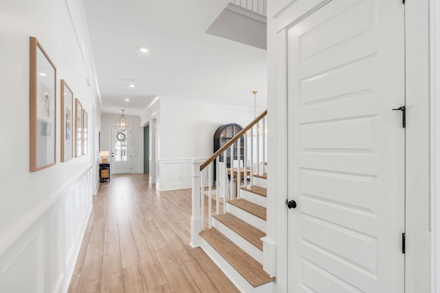 interior space with a notable chandelier, wood finished floors, a decorative wall, crown molding, and wainscoting