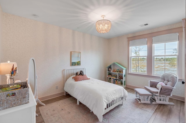 bedroom featuring visible vents, wood finished floors, wallpapered walls, baseboards, and a chandelier