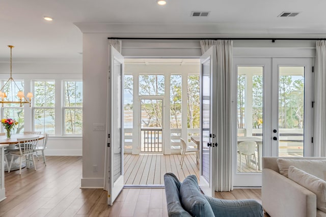 entryway featuring light wood finished floors, visible vents, a notable chandelier, and ornamental molding