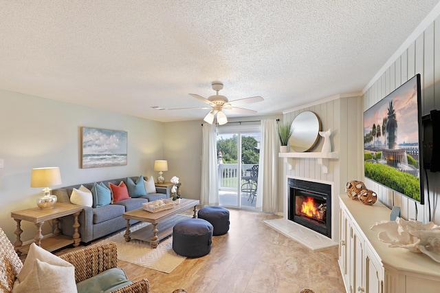 living area featuring a glass covered fireplace, a textured ceiling, and ceiling fan