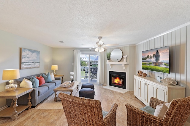 living room featuring a textured ceiling, a glass covered fireplace, and a ceiling fan