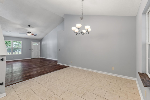 empty room featuring lofted ceiling, a ceiling fan, a chandelier, tile patterned floors, and baseboards