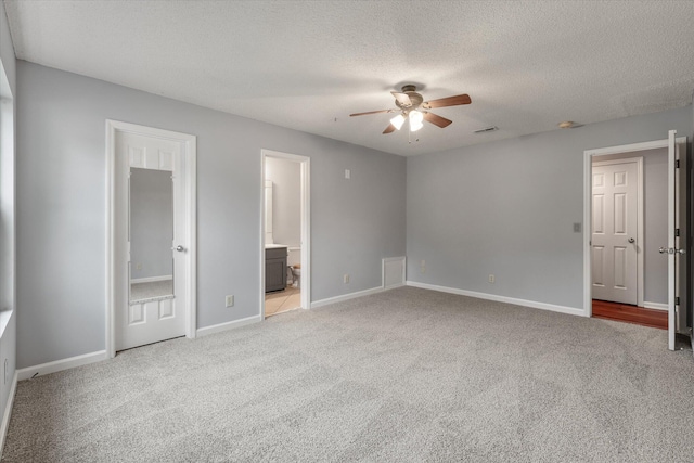 unfurnished bedroom with light colored carpet, a textured ceiling, baseboards, ensuite bathroom, and ceiling fan