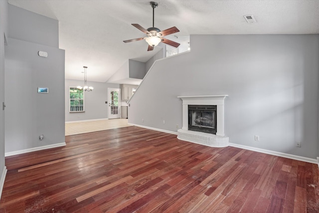 unfurnished living room with a ceiling fan, wood finished floors, a fireplace, a chandelier, and high vaulted ceiling