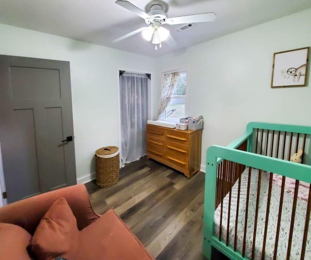 bedroom with ceiling fan, dark wood-type flooring, and a nursery area