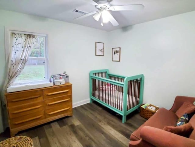 bedroom with a crib, ceiling fan, and dark wood-type flooring