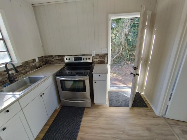 kitchen with a sink, stainless steel range with electric stovetop, decorative backsplash, and light wood finished floors