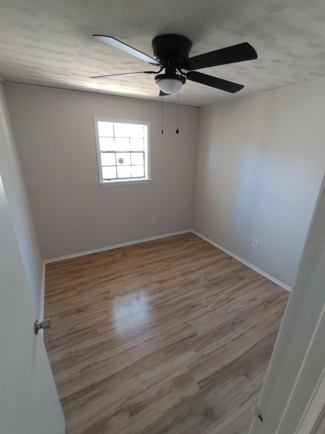 empty room with ceiling fan, wood finished floors, and baseboards