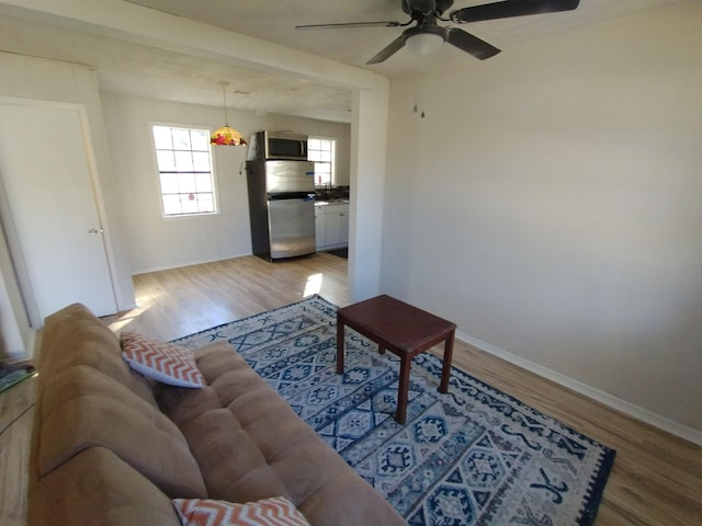 living room featuring light wood-type flooring, ceiling fan, and baseboards