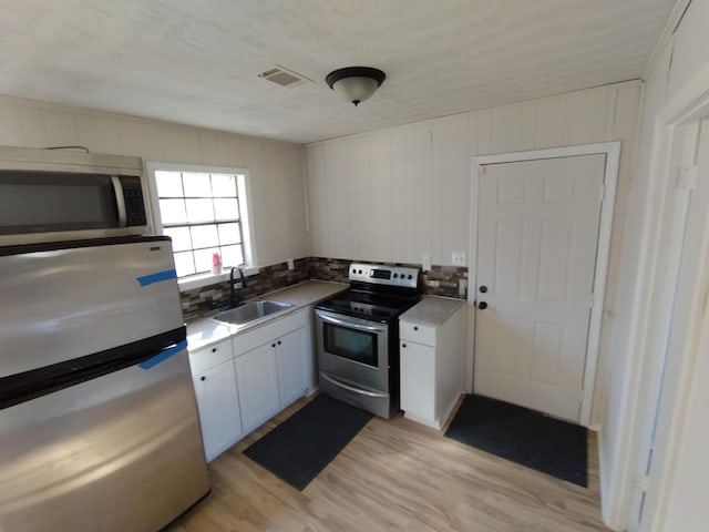 kitchen featuring appliances with stainless steel finishes, a sink, light wood-style flooring, white cabinetry, and tasteful backsplash