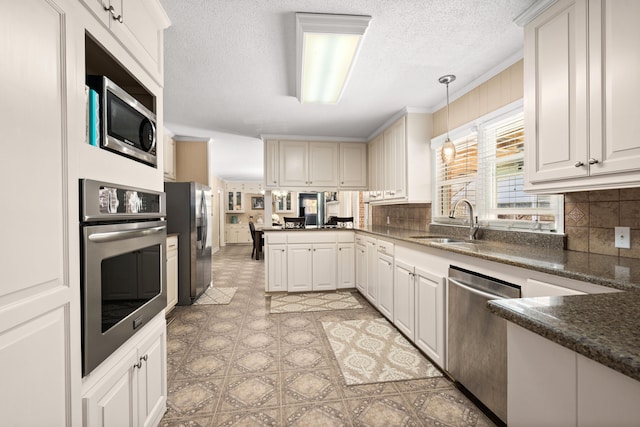 kitchen with sink, appliances with stainless steel finishes, hanging light fixtures, and white cabinets