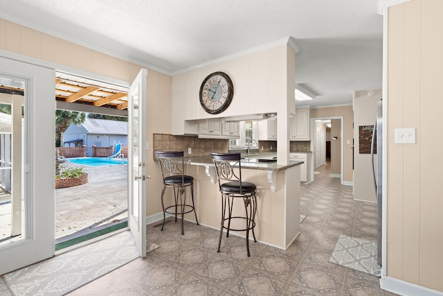 kitchen featuring kitchen peninsula, decorative backsplash, a breakfast bar area, white cabinetry, and ornamental molding