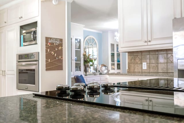 kitchen featuring tasteful backsplash, white cabinetry, dark stone counters, ornamental molding, and stainless steel appliances