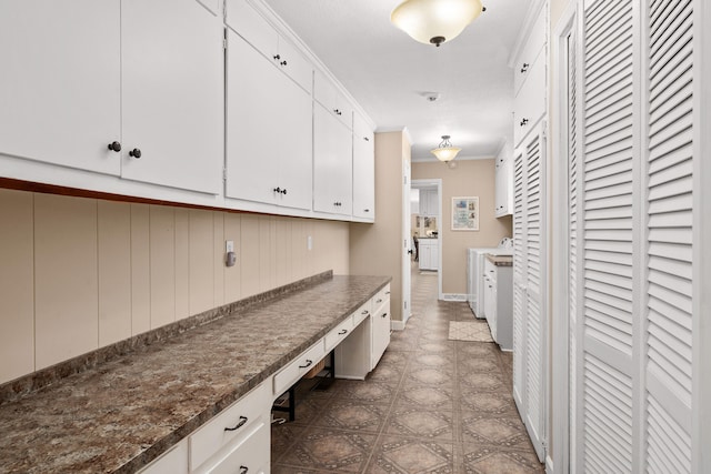 kitchen with crown molding, white cabinetry, and dark stone counters