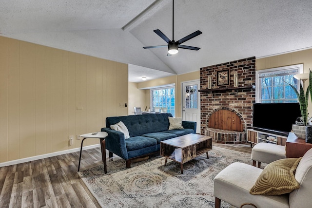 living room featuring a fireplace, vaulted ceiling with beams, a textured ceiling, and wood finished floors