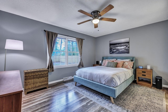 bedroom featuring baseboards, visible vents, a ceiling fan, wood finished floors, and a textured ceiling