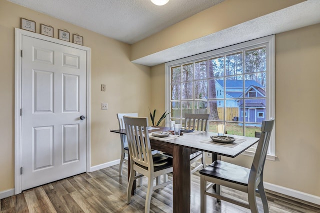 dining area with a textured ceiling, baseboards, and wood finished floors