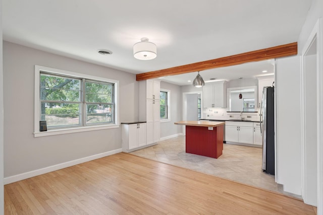 kitchen featuring freestanding refrigerator, a center island, light wood-type flooring, white cabinetry, and a sink