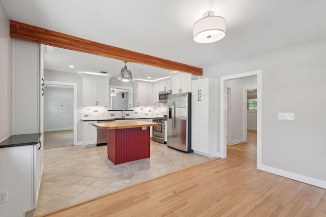 kitchen featuring tasteful backsplash, beam ceiling, white cabinets, stainless steel appliances, and butcher block countertops
