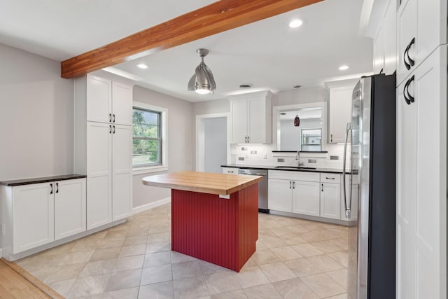 kitchen featuring white cabinets, appliances with stainless steel finishes, beam ceiling, a sink, and backsplash