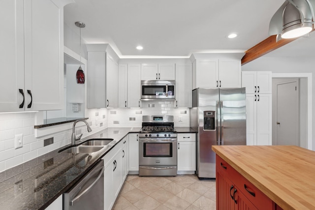 kitchen with appliances with stainless steel finishes, tasteful backsplash, white cabinetry, a sink, and butcher block countertops