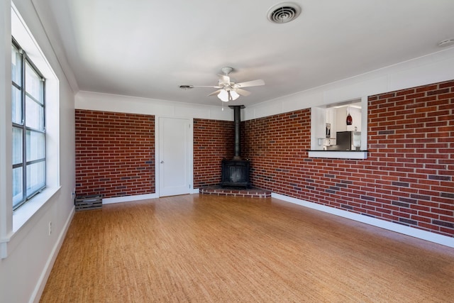 unfurnished living room with baseboards, a ceiling fan, a wood stove, and brick wall