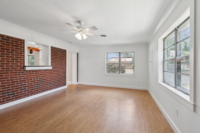 empty room with ceiling fan, brick wall, light wood-style flooring, baseboards, and ornamental molding