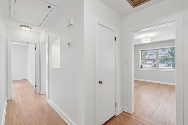 hallway featuring light wood-style floors, baseboards, and attic access