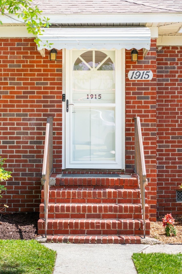 view of exterior entry with a shingled roof and brick siding