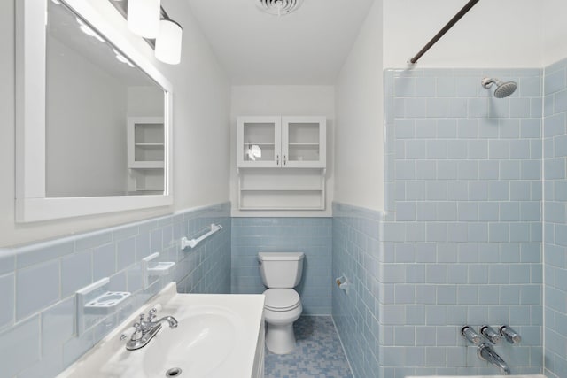 bathroom featuring wainscoting, toilet, tile walls, tub / shower combination, and visible vents
