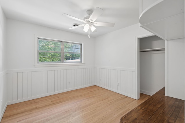 unfurnished bedroom featuring wainscoting, ceiling fan, a closet, and wood finished floors