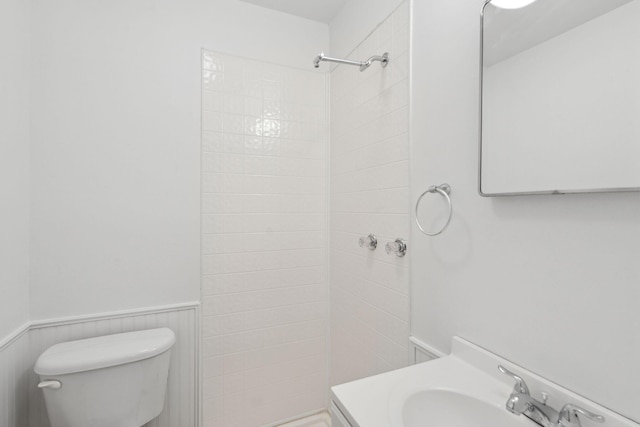 bathroom with wainscoting, vanity, a tile shower, and toilet