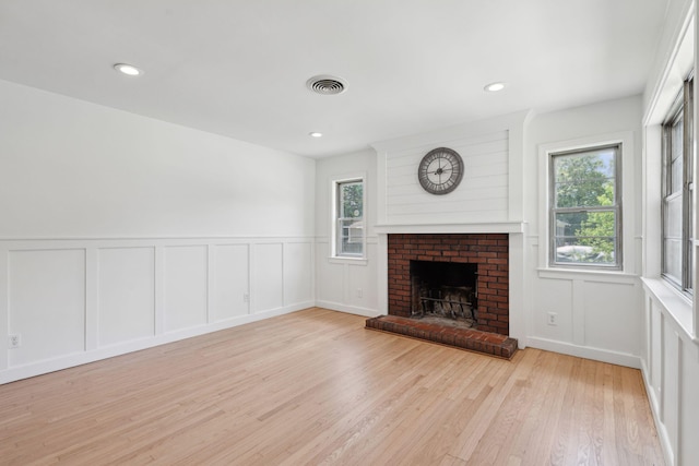 unfurnished living room with a fireplace, a decorative wall, light wood-style flooring, and visible vents