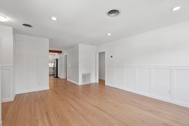 unfurnished living room with light wood-style floors, a decorative wall, and visible vents