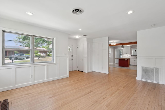 unfurnished living room featuring light wood-style floors, a decorative wall, recessed lighting, and visible vents