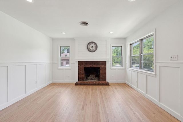 unfurnished living room featuring a brick fireplace, a decorative wall, wood finished floors, and visible vents
