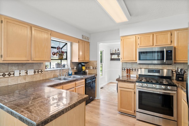 kitchen with light brown cabinetry, appliances with stainless steel finishes, a sink, a peninsula, and backsplash