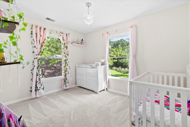carpeted bedroom featuring a chandelier, baseboards, visible vents, and a crib