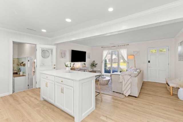 kitchen with a breakfast bar area, white cabinets, ornamental molding, a center island, and light hardwood / wood-style flooring