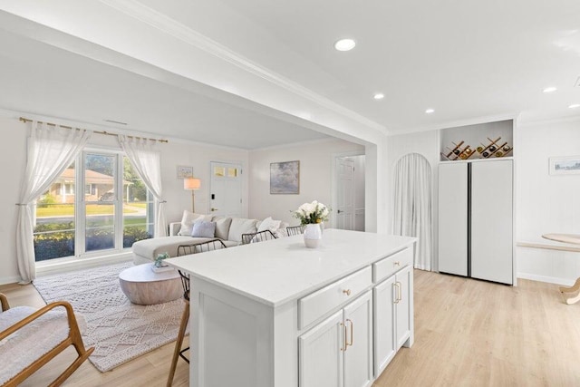 kitchen featuring crown molding, a kitchen island, white cabinets, a kitchen bar, and light wood-type flooring