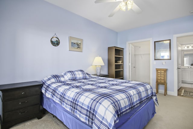 bedroom featuring a walk in closet, a closet, light colored carpet, ensuite bathroom, and baseboards